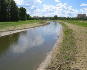 Deserted bank of a small river. Buildings in the distance in the background. Cracked earth. Small bridge in the background