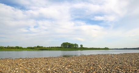 Adorable stone shore by the river. Warm summer day. Trees in the horizon