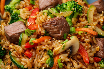 Asian rice with teriyaki beef and vegetables: zucchini, broccoli, pepper, mushrooms, carrot, onion and sesame seeds. Dish isolated in a blue bowl, close-up on a black marble background. Asian cuisine.