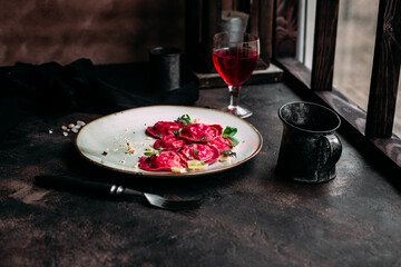 Beetroot ravioli with cheese in a black plate on the table near the window