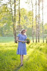 beautiful girl in a blue vintage dress walks in the forest with a bouquet of orange flowers, flower field