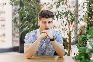 Fototapeta premium A handsome young man with an earring in his ear sits at the table with his hands folded and looks at the camera