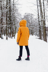 Caucasian woman in an orange jacket in the winter woods, jumping and having fun, enjoying the beauty of nature and enjoying life