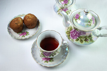 A cup of tea on a white tablecloth. Tea with muffins. Light breakfast. White tea set with flowers.
