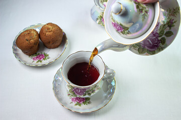 Tea is poured into a cup. A cup of tea on a white tablecloth. Light breakfast. White tea set with flowers.