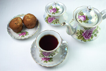 A cup of tea on a white tablecloth. Tea with muffins. Light breakfast. White tea set with flowers.