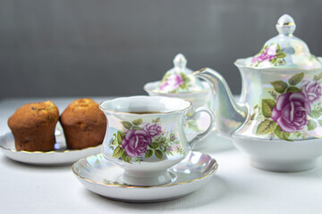 A cup of tea on a white tablecloth. Tea with muffins. Light breakfast. White tea set with flowers.