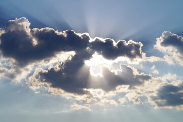 The sun's rays peek out from behind the gray clouds in the sky