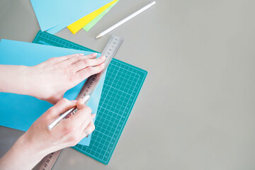 Women's hands are cutting blue paper for a lesson from postcards. The