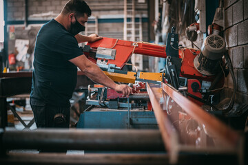 an adult man working with a metal cutting machine in an industrial warehouse