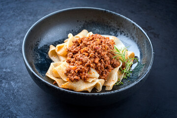 Modern style traditional Italian ragu alla bolognese sauce with papedelle pasta noodles and parmesan cheese served as top view in a ceramic design bowl with copy space
