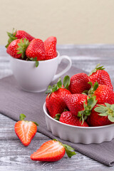 Juicy strawberries in a white ceramic bowl and cup on a gray shabby wooden table in a rustic style. Vertical photo