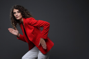 Portrait of a girl in a red jacket and white trousers on a gray background