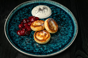 Fototapeta na wymiar Cheesecakes with sour cream, cherry jam on a dark wooden table 