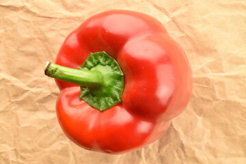 One red bell pepper on craft paper, close-up, top view.