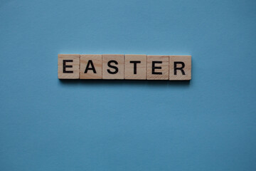 wooden letters with the inscription (easter), light wooden letters on a blue background. Flat lay