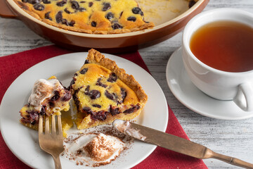 Fresh slice of cherry pie with ice cream and white cup with tea on a wooden background