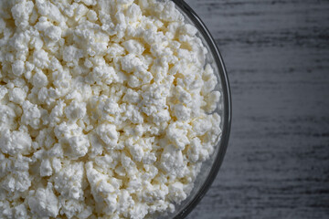 Cottage cheese in glass bowl of background, top view. White grainy texture of dairy product