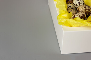 Quail eggs in a white box on yellow paper, minimalism. elegant easter background, space for text, copy space,