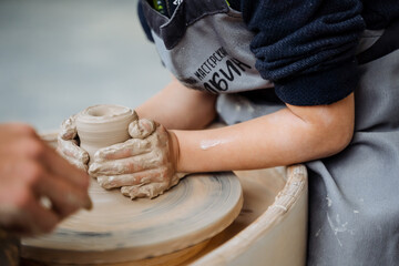 The child is engaged in a potter's wheel. Pottery Workshop. sculpt from the clay pot. creativity for children. fine motor skills of the hands. four hands.