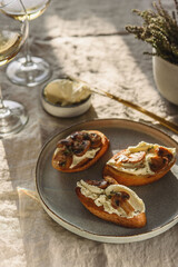 Fototapeta na wymiar Bruschettas or toasts with cheese and fried mushrooms with thyme served with glasses of wine on greige linen tablecloth