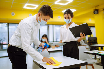 Office worker in protective sterile mask and gloves cleans the working desk with the wiping cloth...