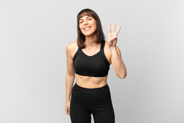 athlete woman smiling and looking friendly, showing number three or third with hand forward,...