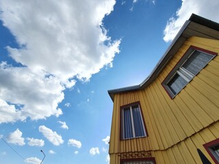 A building with yellow walls against a clear sky. Small windows look out onto the street, offering a view of the clear sun.