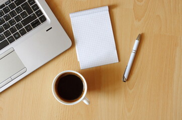 Laptop with coffee cup, notebook and pen on wooden background Top view. Concept for home office. Business concept. Work from home. Desk with laptop, blank notepad, coffee cup and pen on wooden table.