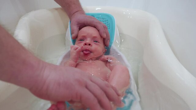 Bathing newborn baby in a baby bath, father bathing his 3-week-old son, infant in baby bath seat support.
