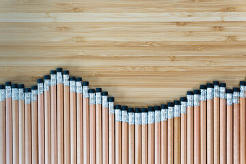 Top view of several pencils located in row on wooden table. Sharp pens laying in chaotic order. Tool for drawings on paper. Equipment
