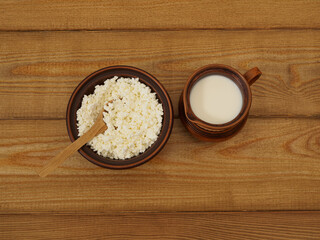Healthy rural breakfast with natural dairy products in handmade crockery top view, flat lay. Homemade natural cottage cheese in a clay bowl and cow's milk in a clay jug on a wooden table. Pottery