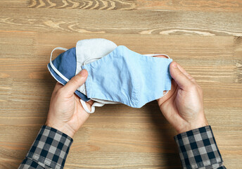 hands with selfmade breathing mask on a wooden background, checkered shirt in rustic style, health...
