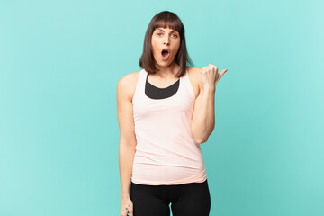 athlete woman looking astonished in disbelief, pointing at object on the side and saying wow,...