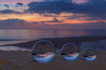 Three clear crystal balls of three sizes are sphere reveals  seascape view with spherical .placed on the sand at Karon Beach during sunset.