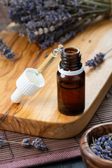 organic cosmetics concept, glass bottle with oil, pipette and lavander flowers on light wooden background