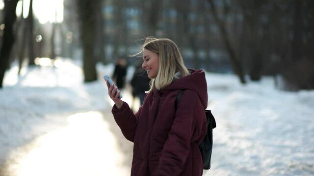 Young blonde woman is very happy to read good news on phone while walking in the city park. Girl jumping and dancing happily