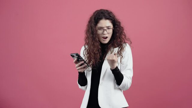 The enthusiastic young woman orders online with her phone and bank card. Young hipster in white jacket and black shirt,