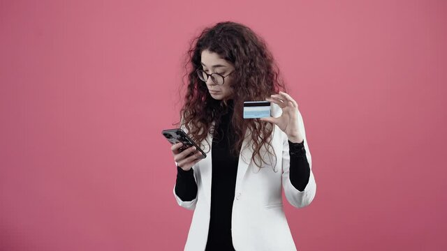 Mature young woman with curly hair, shopping online with the phone, enters the number on the card. Young hipster in white jacket and black shirt,