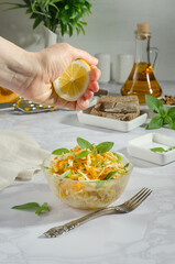 Woman squeezes lemon into a salad of cabbage, grated carrot with basil and rosemary