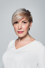 portrait of middle aged woman in white blouse looking at camera isolated on grey