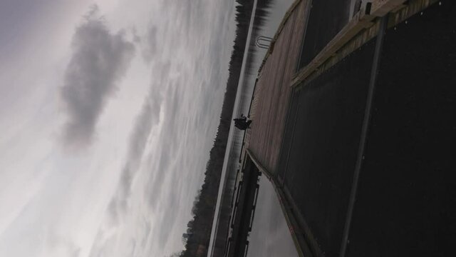 Rotating towards a Man using a DLSR camera mounted on a gimbal to record film scenery of a lake at a park with sky trees clouds reflecting off of surface of lake water