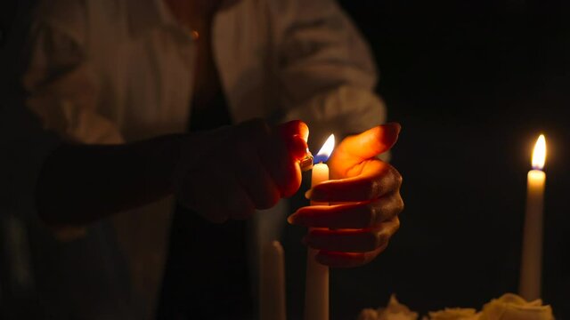 Closeup hands of woman lighting candles in elegant restaurant. Romantic dinner concept and celebrating. Dark background