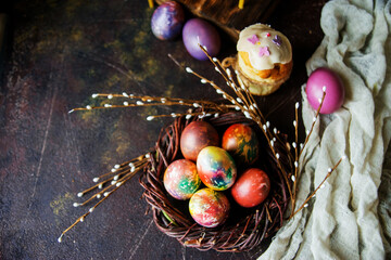 Fototapeta na wymiar Colorful Easter eggs in a decorative nest, next to willow branches on a dark background, a copy of the space