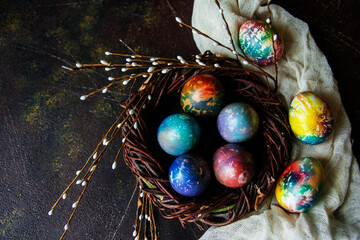 Colorful Easter eggs in a decorative nest, next to willow branches on a dark background, a copy of the space