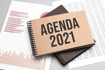 Notepad with text Agenda 2021 on a white background, near laptop, calculator and office supplies. Business concept.
