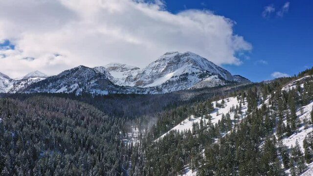 Aerial View Over Canyon With Wind Blowing Snow Through The Trees Viewing Timpanogos Mountain In Winter.