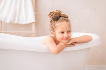 Obraz na płótnie Canvas Baby girl sitting in the bathroom. Portrait of a cute girl in sunglasses in a bright bathroom.