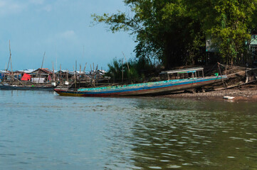 Traditionelles hölzernes Fischerboot in Asien, es liegt zum Teil auf dem Trockenen, im Hintergrund ein Fischerdorf