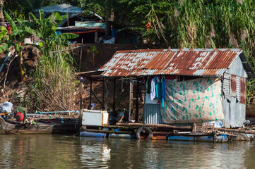 Blick vom Mekong auf den Uferbereich. Dieser ist gesäumt mit typischen Stelzenbauten und Hausboote n, gebaut aus Wellblech.   